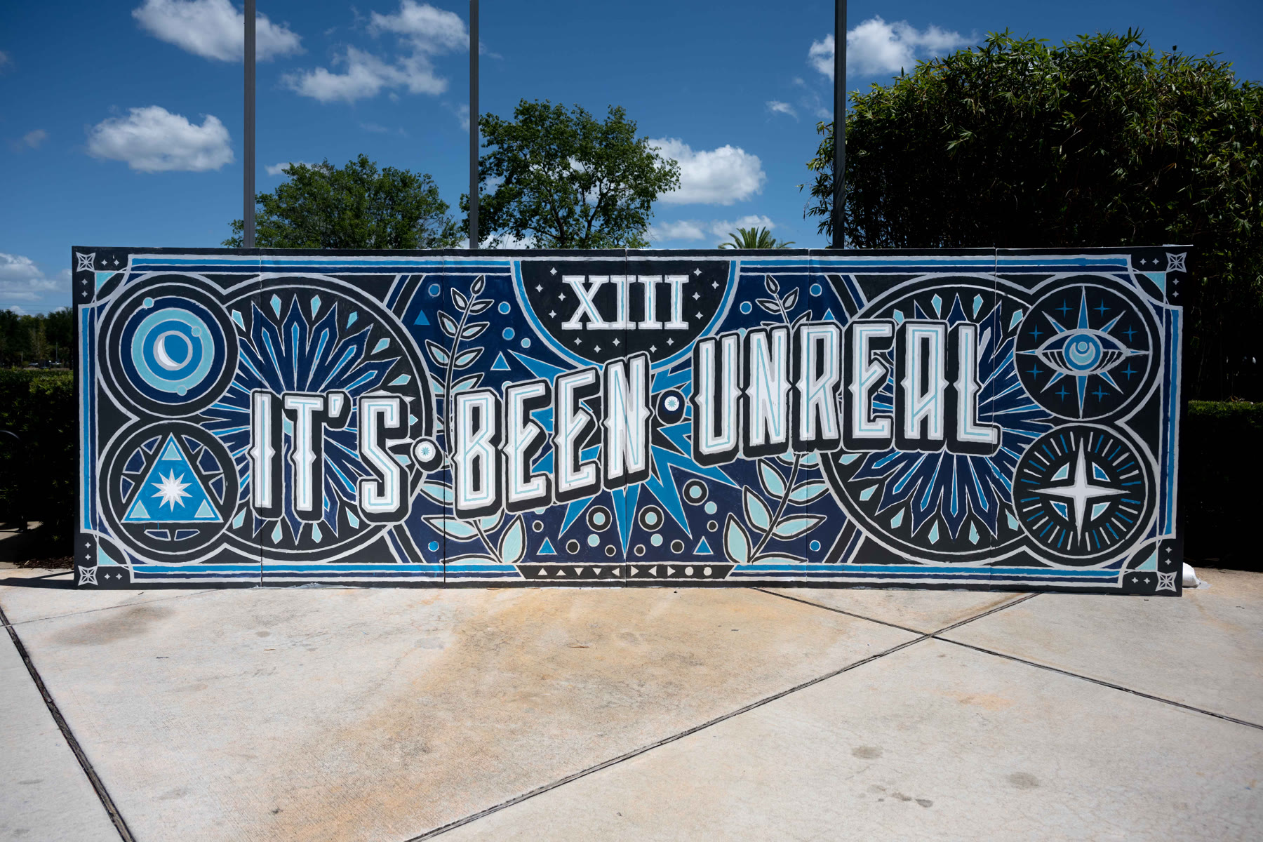 The It’s Been Unreal mural installed outdoors: ornate navy and white lettering with celestial icons